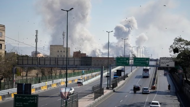 מכוניות נוסעות בכביש באיראן, כשברקע פטריות עשן