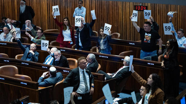 חברי האופוזיציה מניפים שלטים עם מספר החטופים בהצבעה על התקציב