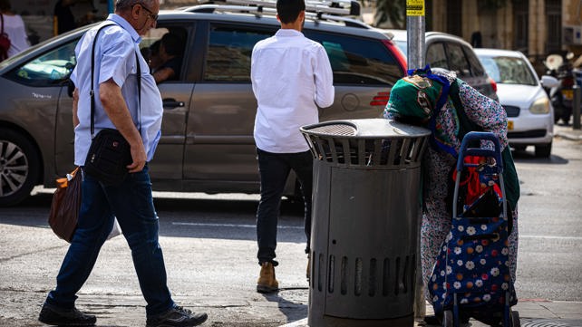 אישה מבוגרת מחפשת פחיות בפח אשפה