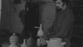 אדם עומד לצד כלי קרמיקה שהכין. 1.1.1976